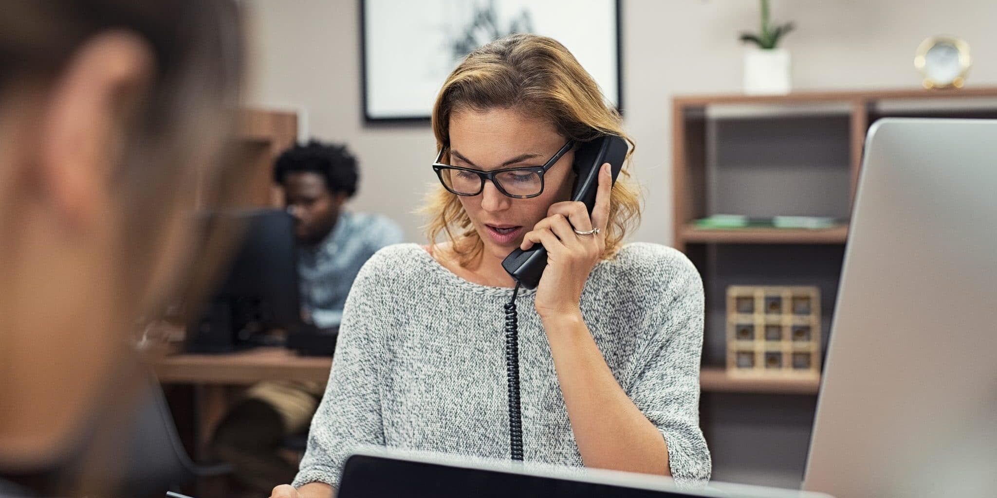 Mature businesswoman talking on phone in office. Casual business woman talking on landline phone in a creative agency. Beautiful blonde receptionist with eyeglasses taking client details over phone.